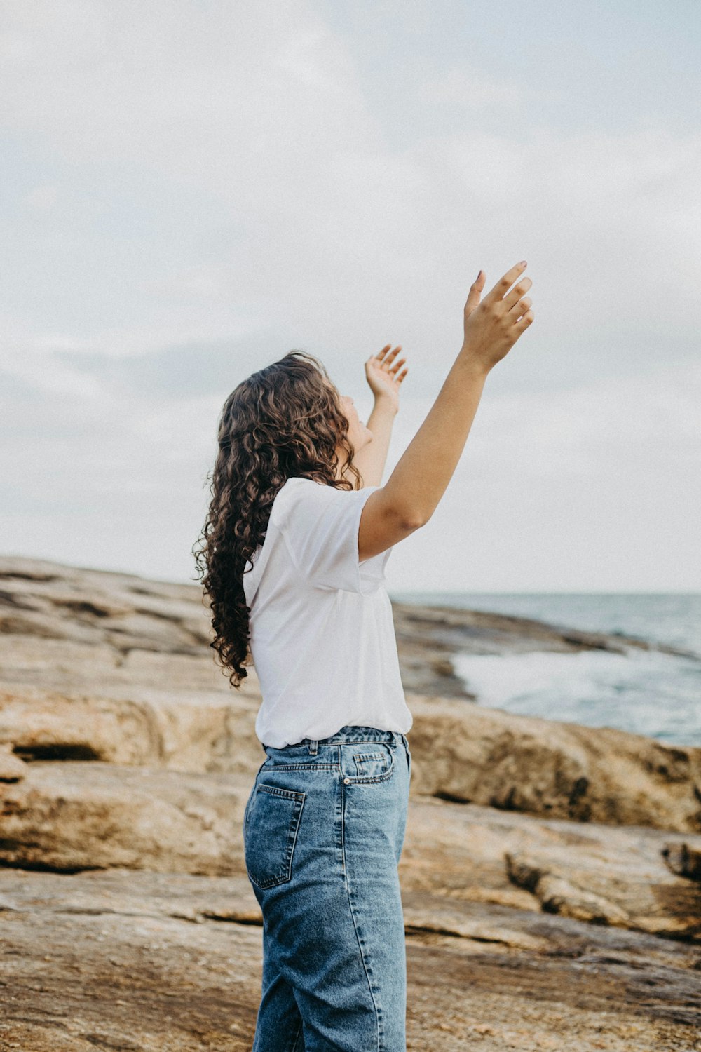 a woman standing on top of a rocky beach next to the ocean