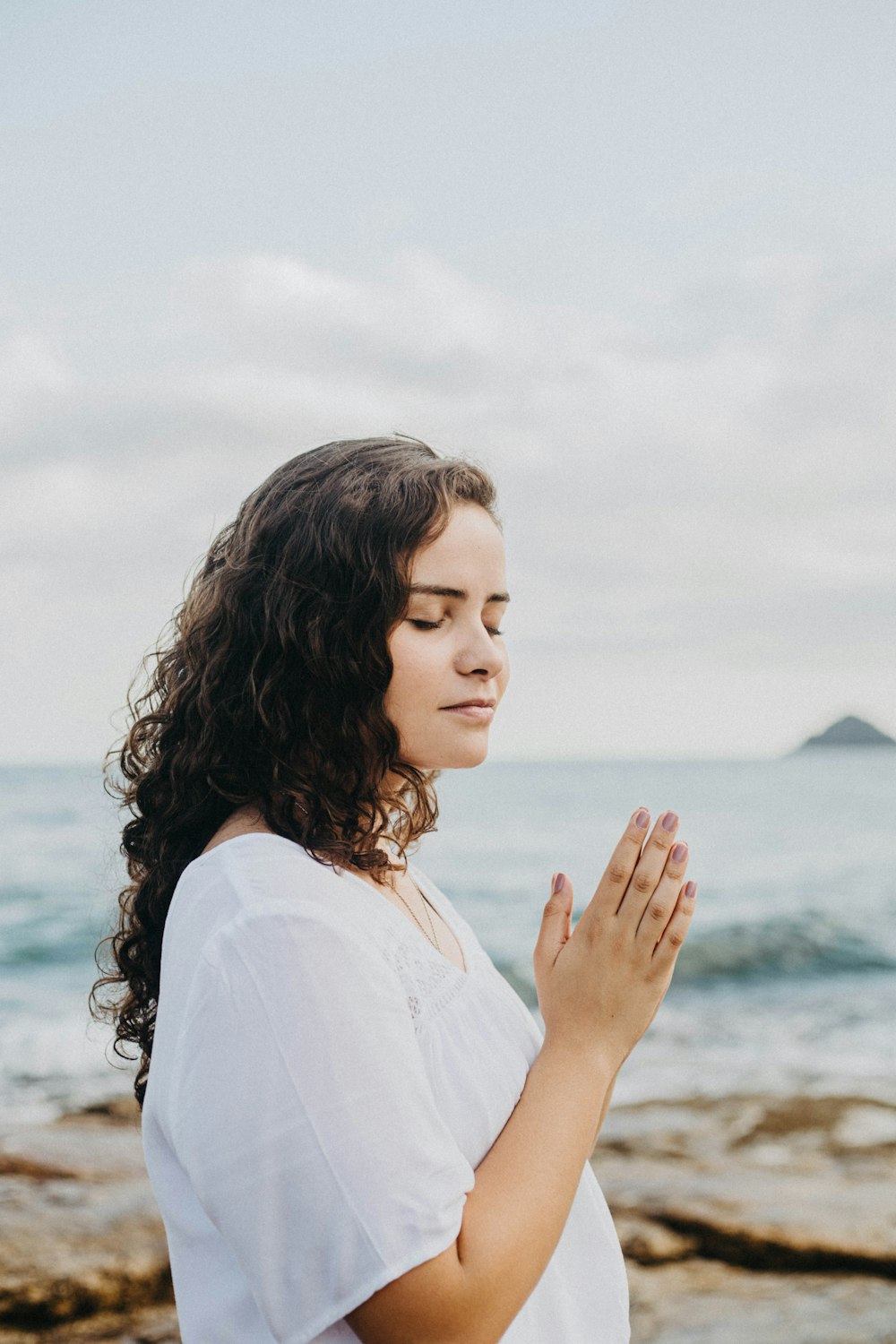 a woman standing in front of the ocean praying