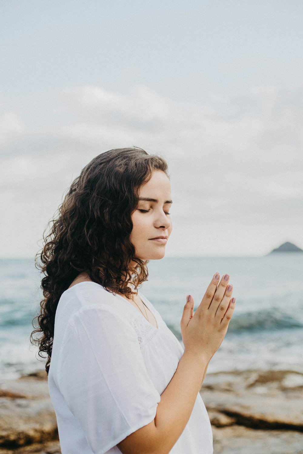 Una mujer de pie frente al océano rezando