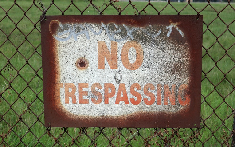 a rusted no trespassing sign on a chain link fence