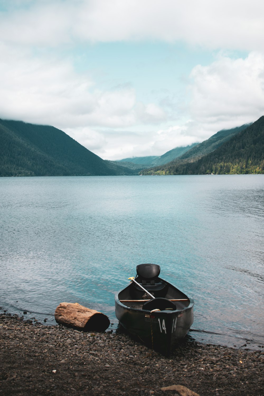 a boat on the shore of a lake with mountains in the background