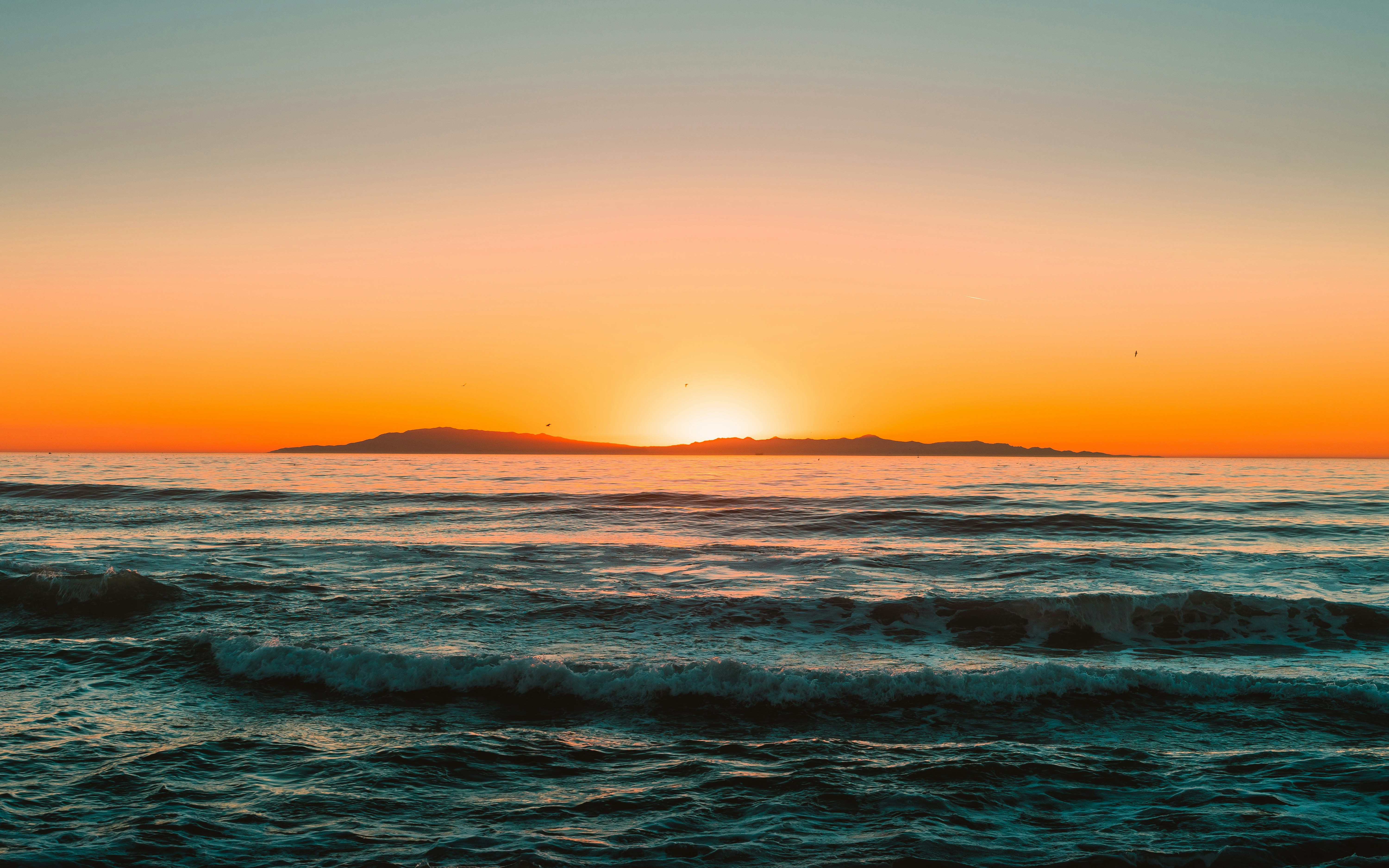 a sunset over the ocean with a small island in the distance