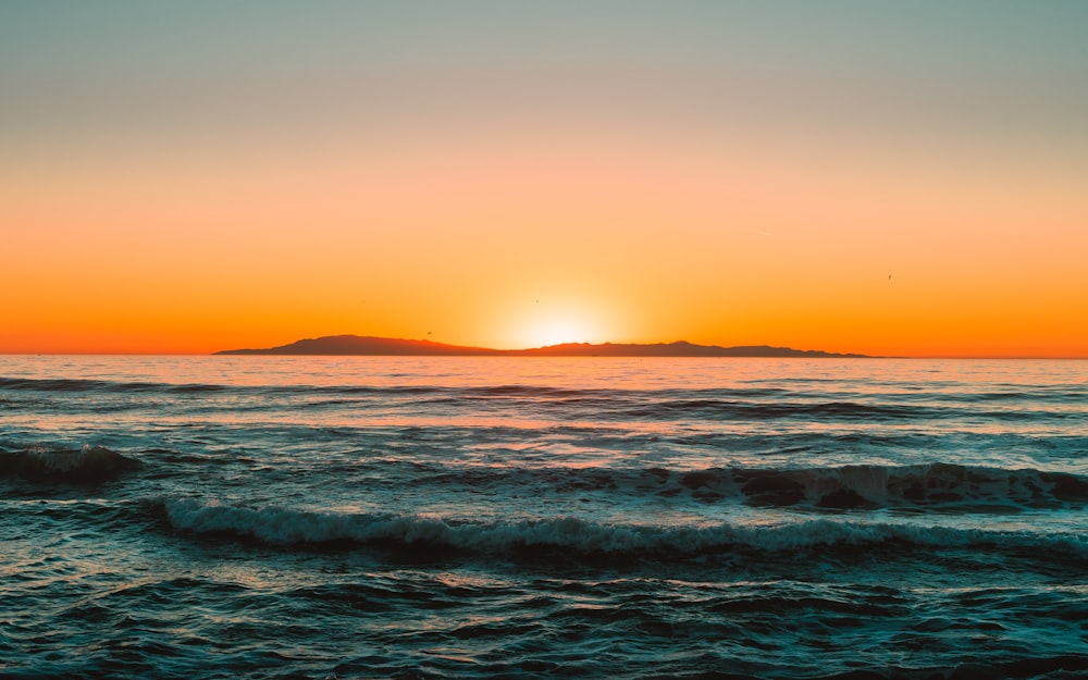 a sunset over the ocean with a small island in the distance