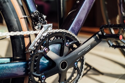 Close-up of a bicycle crankset featuring a chainring, chain, and pedal. The frame and components have a sleek, metallic finish.