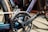 Close-up of a bicycle crankset featuring a chainring, chain, and pedal. The frame and components have a sleek, metallic finish.