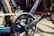 Close-up of a bicycle crankset featuring a chainring, chain, and pedal. The frame and components have a sleek, metallic finish.
