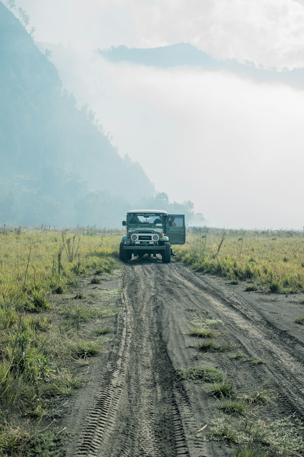 a truck driving down a dirt road in the middle of a field