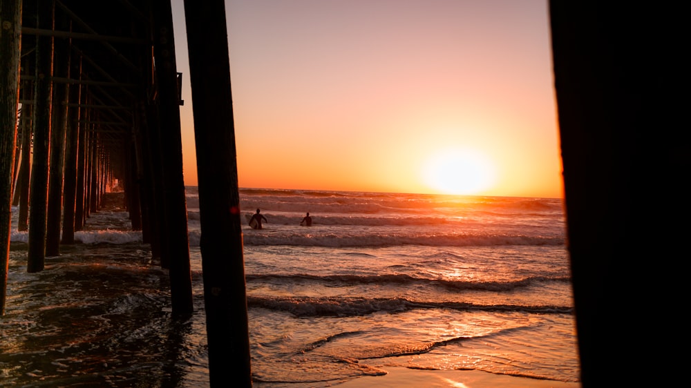 the sun is setting over the ocean and a pier