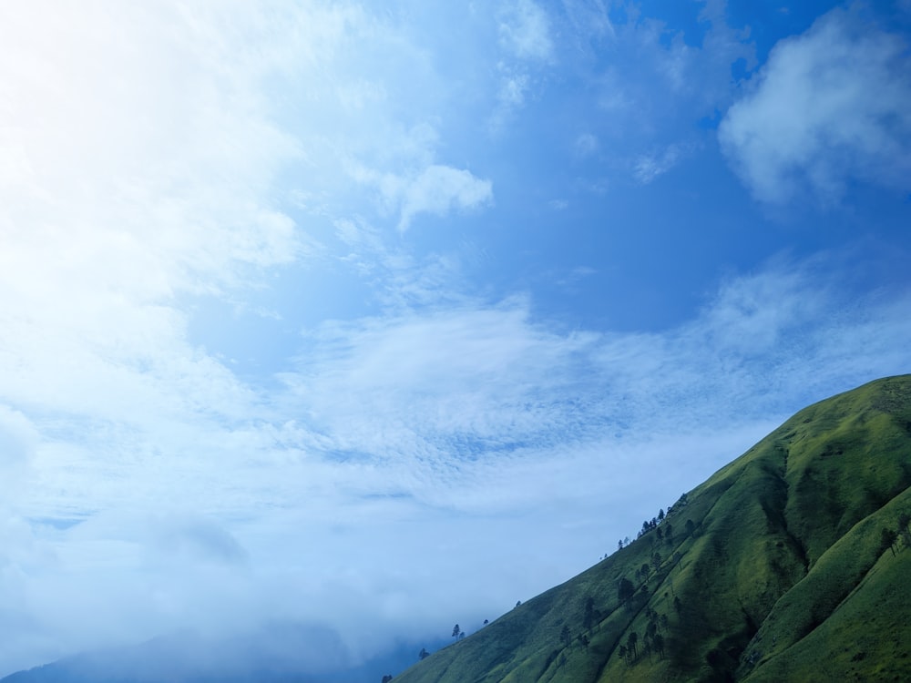 a green mountain with a few clouds in the sky