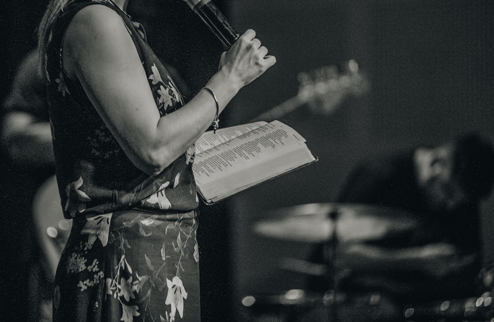 a woman holding a book while standing in front of a microphone