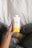 A hand is holding a tetra pak carton of Après Vanilla Bean flavored plant protein drink. The person holding the drink is wearing grey sweatpants and is sitting on a soft, white surface.