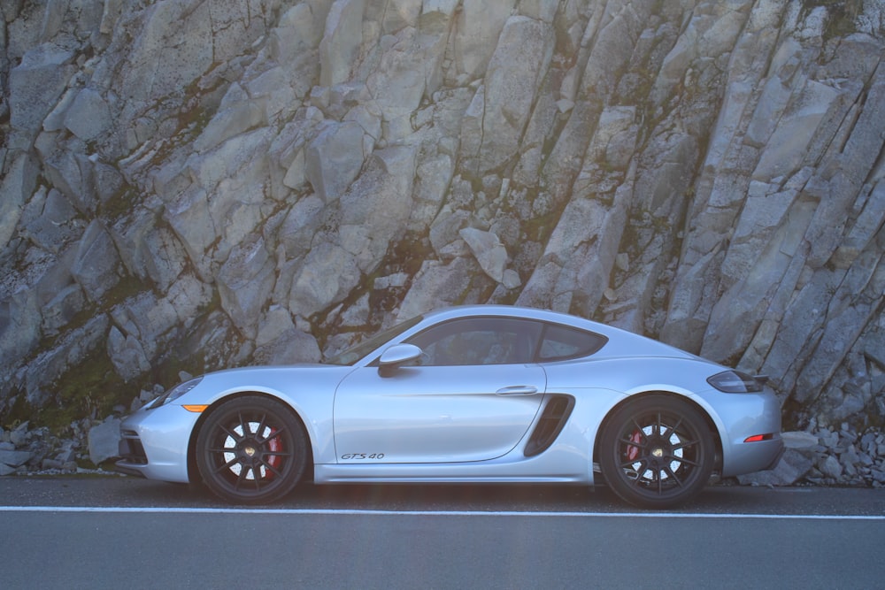 a silver sports car parked in front of a rock wall