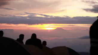 Sunset view from a mountain peak with club members silhouetted against the sky.