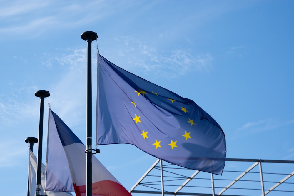 two flags flying next to each other in front of a blue sky