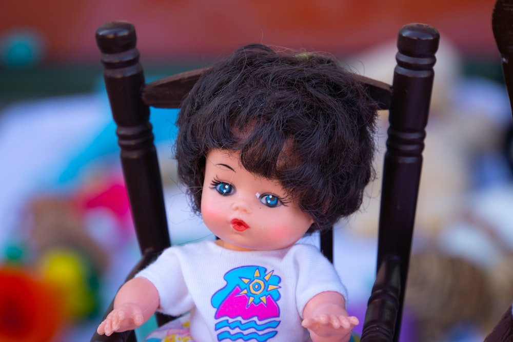 a doll sitting in a chair with a t - shirt on