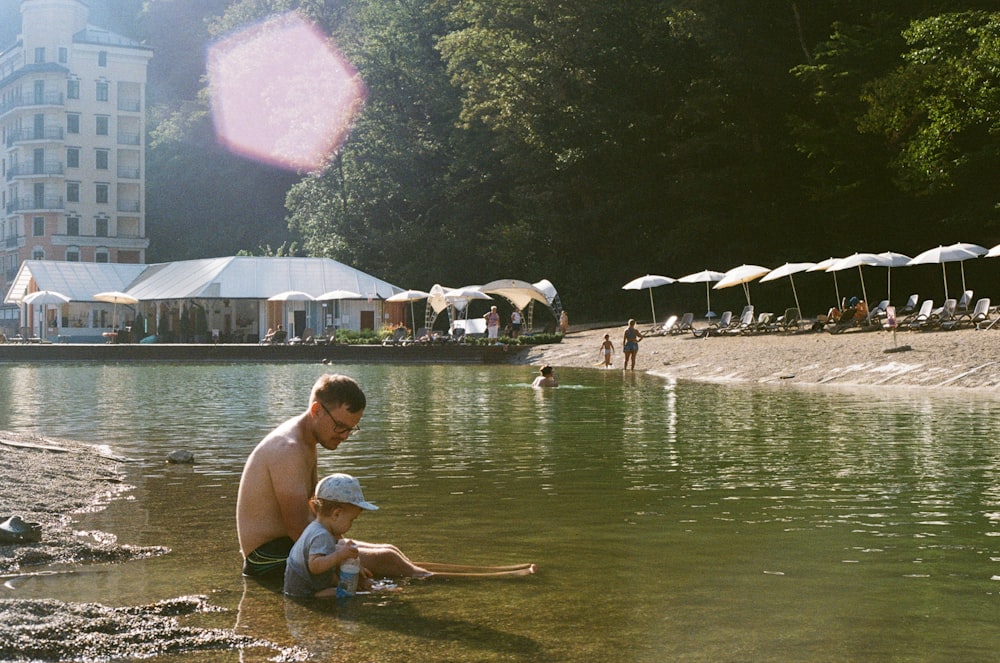 a man and a child sitting on the shore of a lake