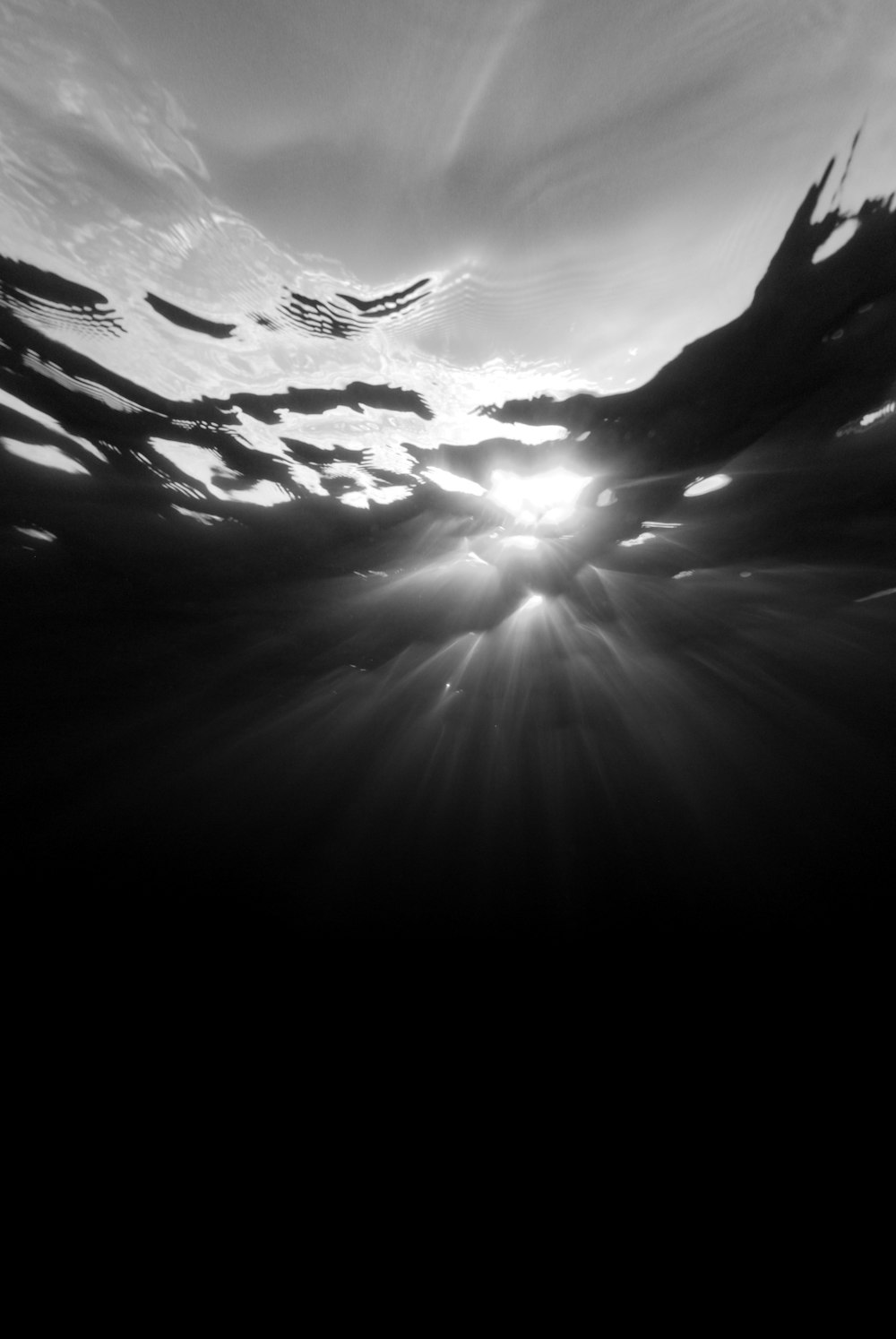 a black and white photo of the sun shining through the water