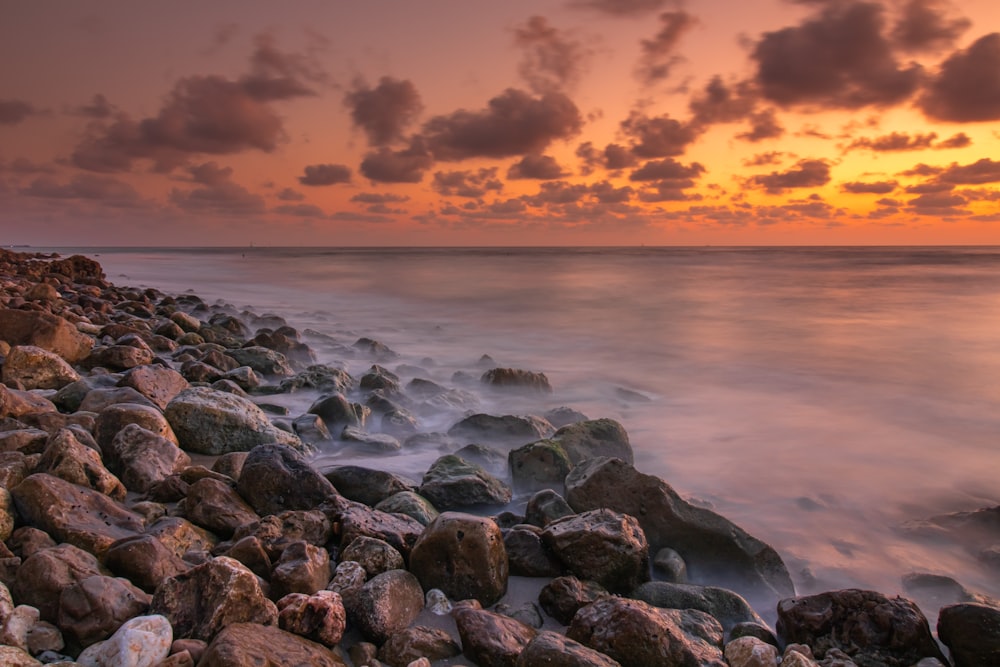 the sun is setting over a rocky beach