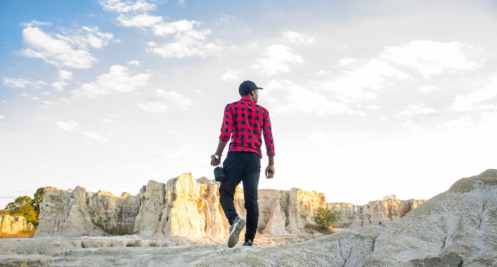 a man in a red and black shirt is walking on a rock