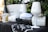 A still life arrangement featuring bottles of Maïa sparkling wine, two white wine glasses with the Maïa logo, a white bucket, and a cap with the word 'Signorvino' on it. The items are set against a backdrop of greenery, creating an elegant and sophisticated atmosphere.