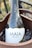 A bottle of wine labeled 'MAÍA BENACUS' rests in a wooden ice bucket. The bottle's design features a constellation pattern over a night sky background. The text 'GARDA DOC' is displayed on the neck of the bottle.