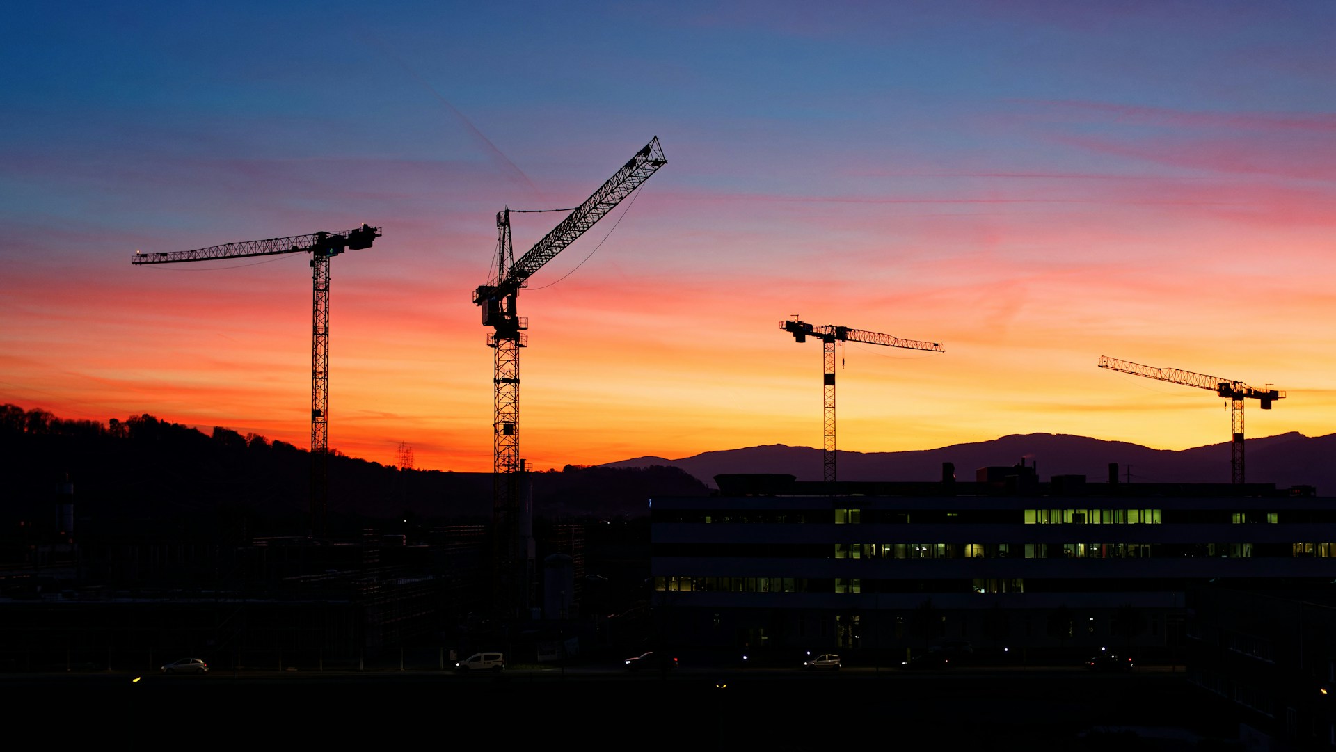a group of cranes are silhouetted against a sunset