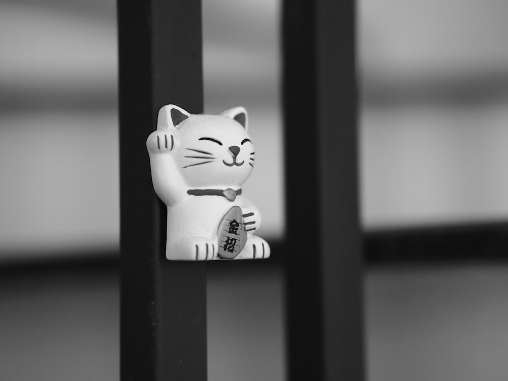 a white cat figurine sitting on top of a metal pole