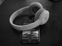 A pair of over-ear headphones rests on top of a smartphone displaying an advertisement for a vehicle, with both items set against a dark, smooth surface. The scene creates a minimalist and modern aesthetic.
