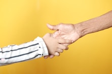 a person holding a child's hand with a yellow background