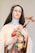 A statue of a woman wearing a veil and a habit, holding a crucifix in one hand and a bouquet of colorful roses in the other. The expression is serene and contemplative.