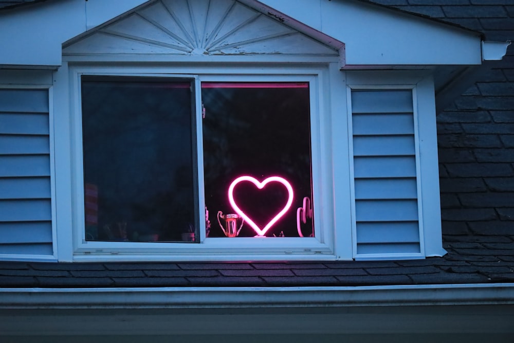 a heart - shaped neon sign in a window of a house