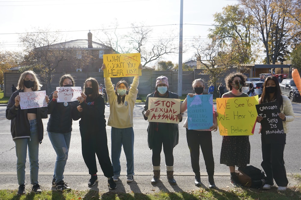 a group of people standing on the side of a road holding signs