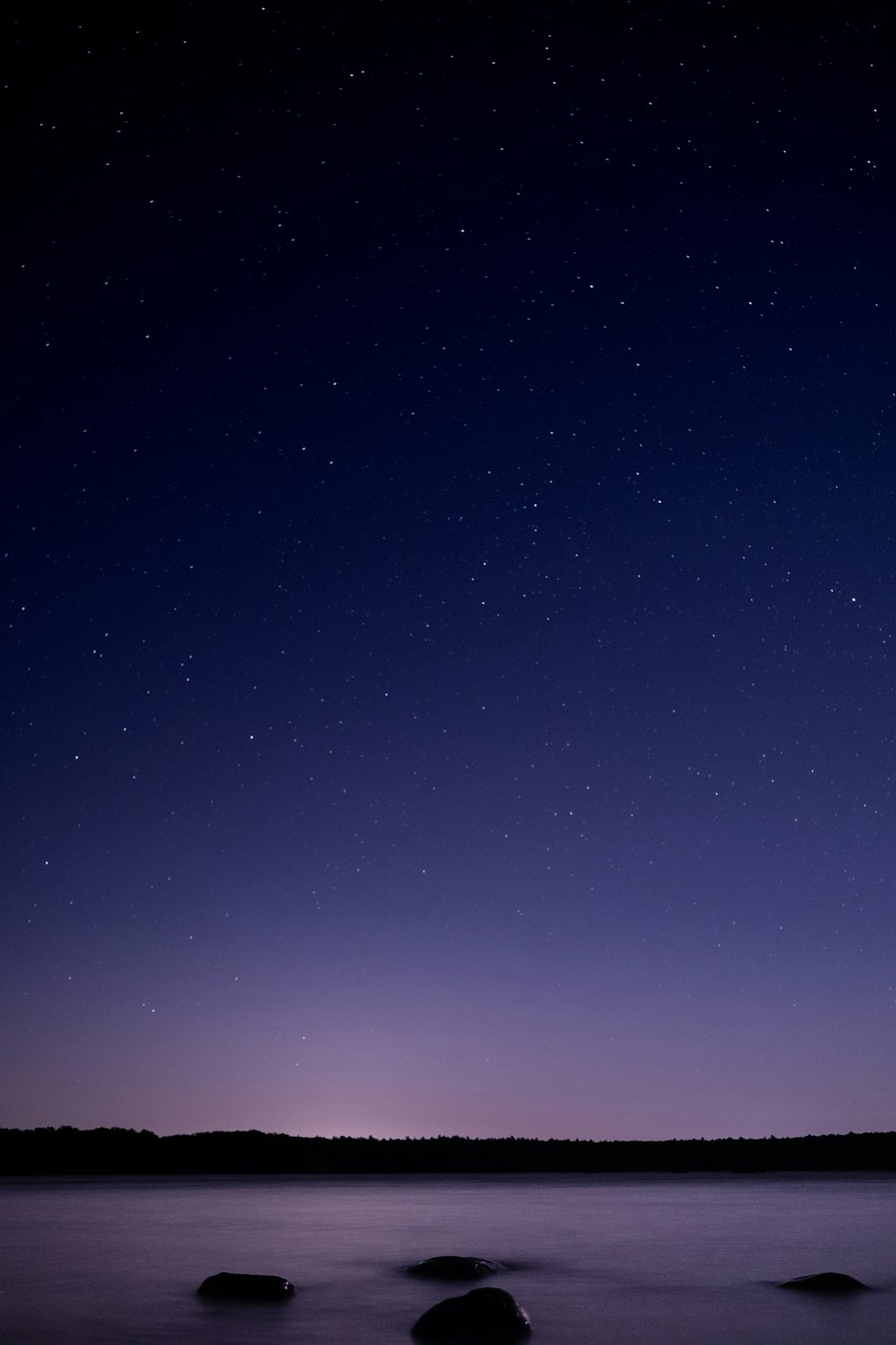 a night sky with stars above a body of water