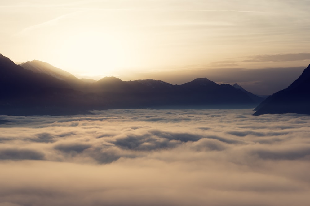 the sun is setting over the mountains above the clouds