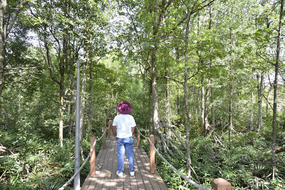 a woman walking across a wooden bridge in a forest