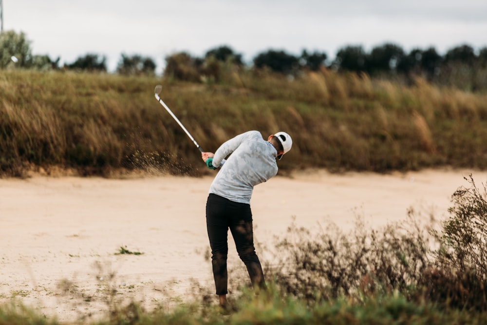 a man swinging a golf club on top of a sandy beach