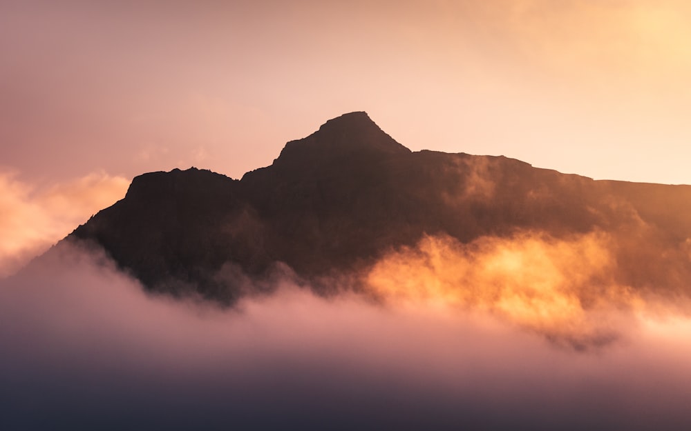 uma montanha coberta de nevoeiro e nuvens ao pôr do sol