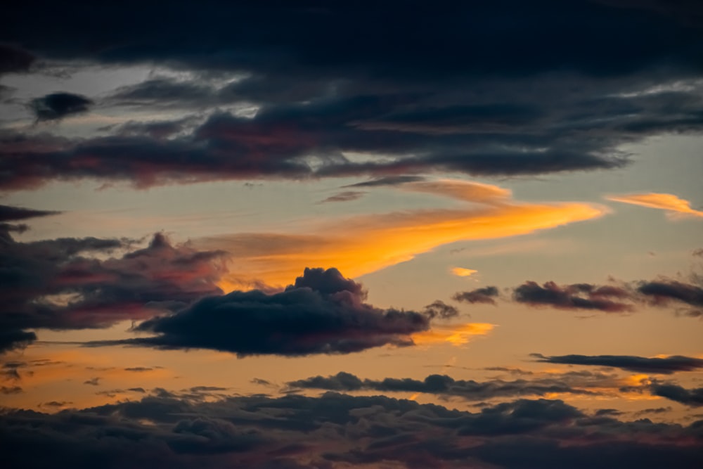 a plane flying through a cloudy sky at sunset