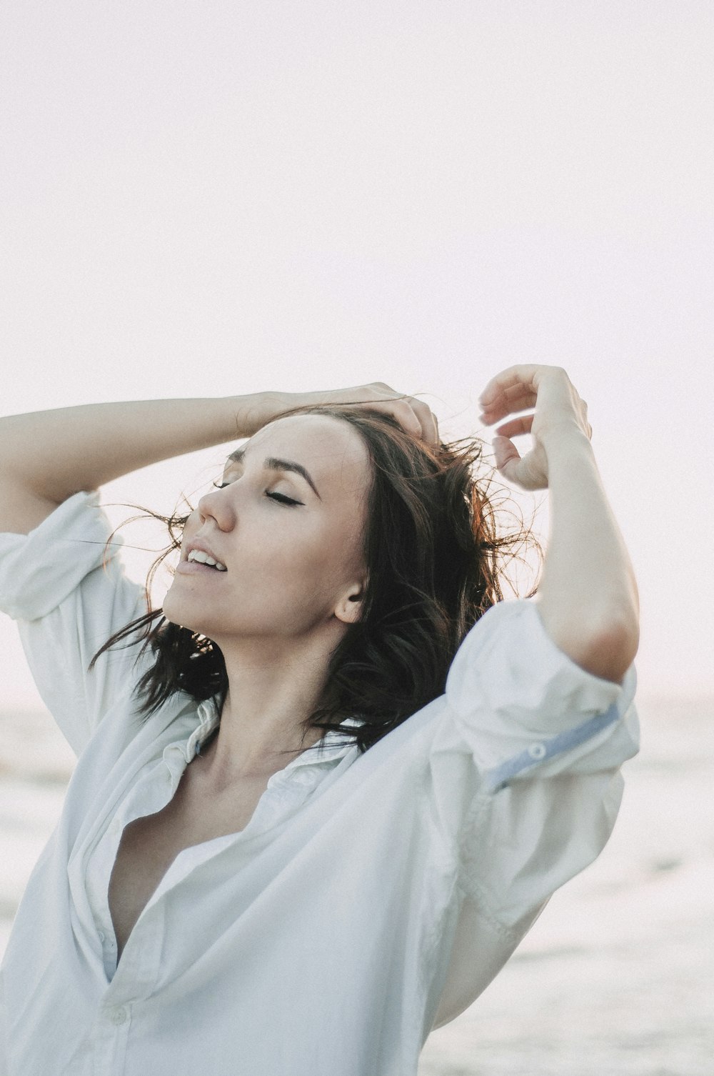 a woman standing on a beach holding her hair in the wind