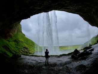 a person standing in a cave with a waterfall in the background