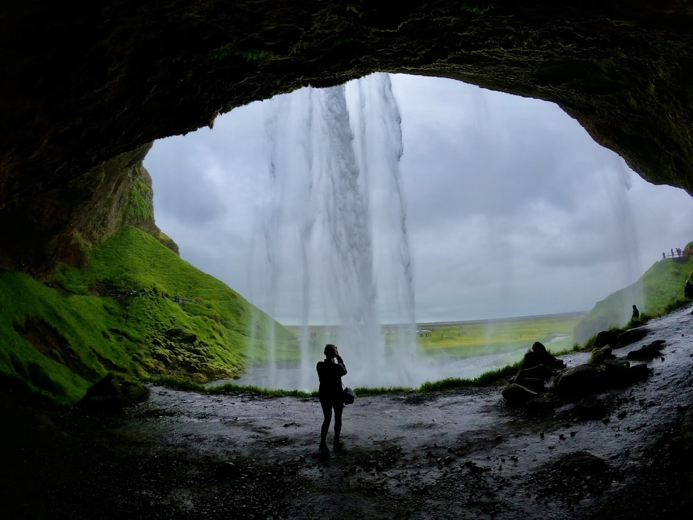 a person standing in a cave with a waterfall in the background
