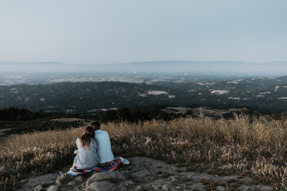 two people sitting on top of a hill