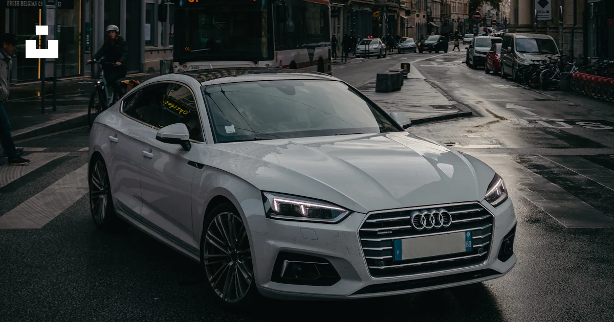 A white car driving down a street next to tall buildings photo – Free ...