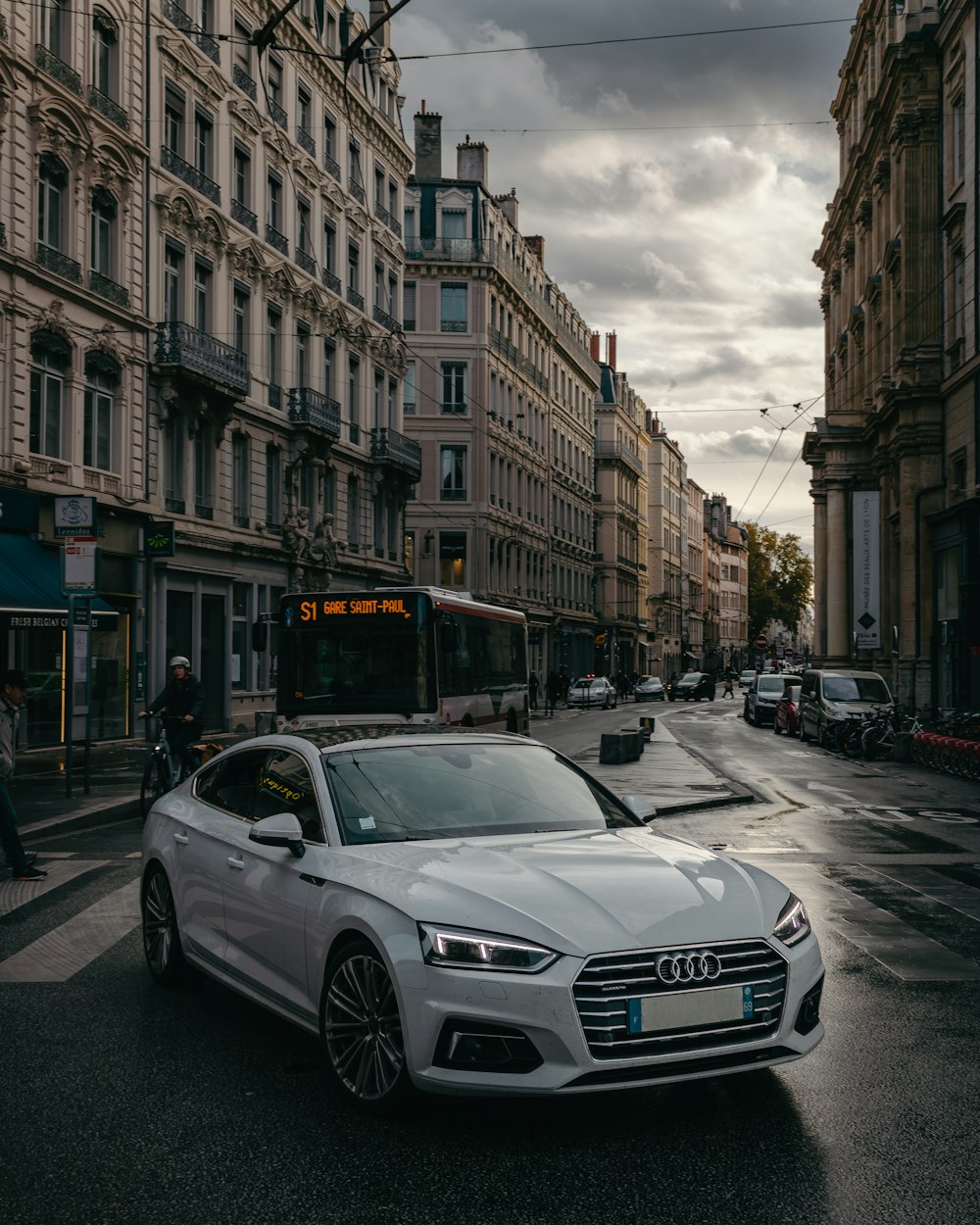 a white car driving down a street next to tall buildings