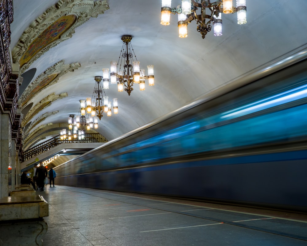 a train passing by a subway station with chandeliers hanging from the ceiling