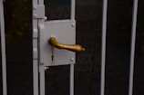 A close-up of a rusty, golden door handle attached to a white metal gate, with a visible keyhole beneath the handle.