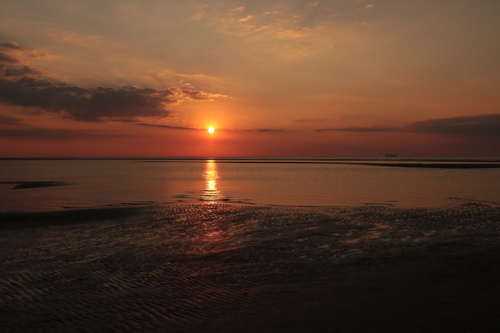 the sun is setting over the water on the beach