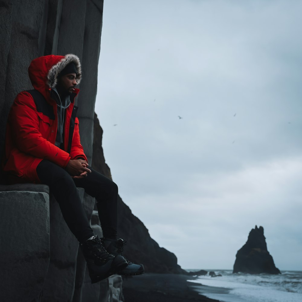 a man in a red jacket is sitting on a ledge