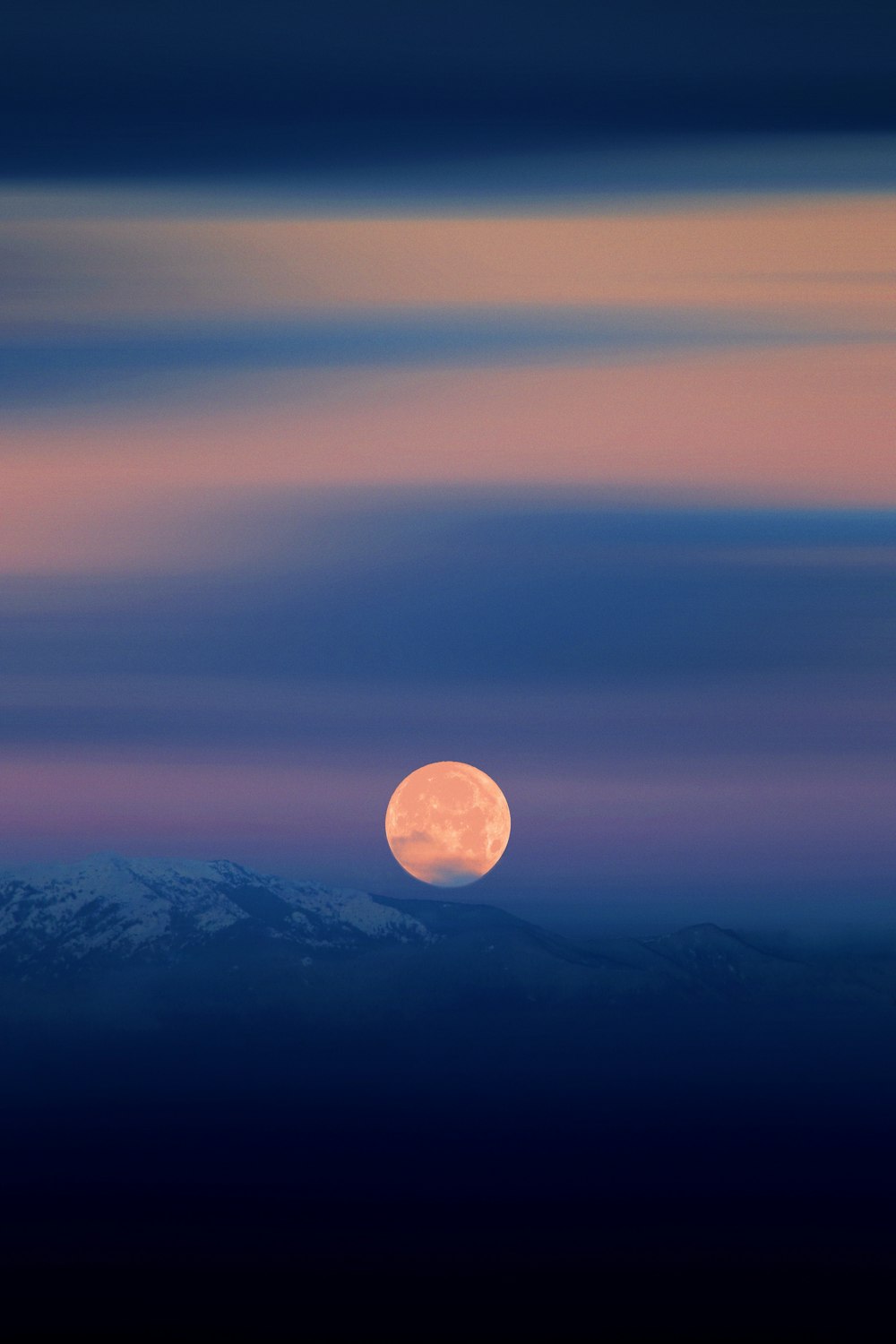 a full moon rising over a mountain range