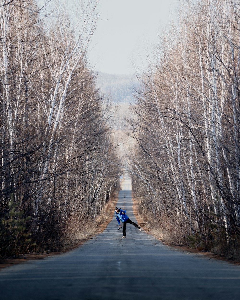 uma pessoa em pé no meio de uma estrada cercada por árvores